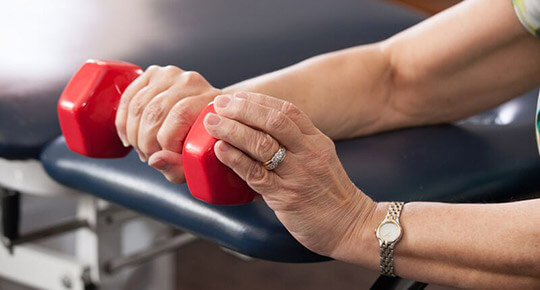 physical therapy patient holding red dumbbell